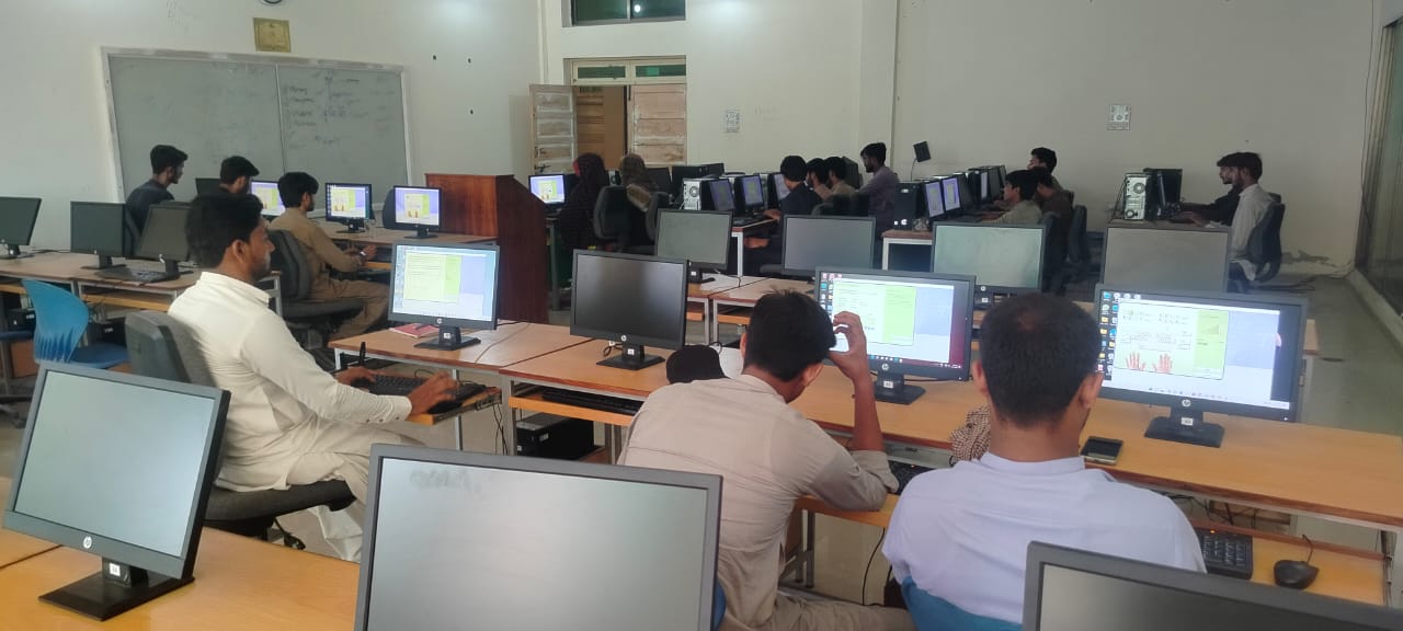 Front view of a historic university building with a prominent statue under a clear sky.